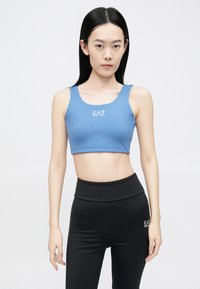 Világoskék crop top logóval, magasan szabott fekete leggingsszel párosítva, mindkettő sima, rugalmas anyagból készül.