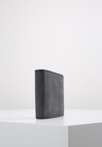 Portefeuille en cuir gris avec une texture lisse, de forme rectangulaire et des coutures visibles le long des bords. Debout sur une surface blanche.