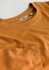 Oranges T-Shirt aus Baumwolle mit Rundhalsausschnitt, kurzen Ärmeln und einer Brusttasche. Glatte Textur, präsentiert in gefalteter Position.