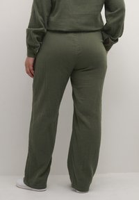 Olivegrüne, strukturierte, leichte, lässige Hose mit geradem Bein und dezenten Falten, kombiniert mit weißen Schuhen.