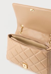 Béžová kožená kabelka so vzorom prešívania, zlatými kovaniami a retiazkovým remienkom. Interiér obsahuje vrecko so zipsom a béžovú podšívku.