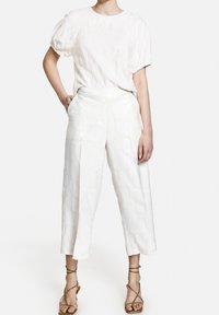 Biała teksturowana bluzka z krótkimi bufkami zestawiona z białymi, szerokimi spodniami o subtelnym wzorze. Sandały na cienkich paskach w kolorze brązowym.