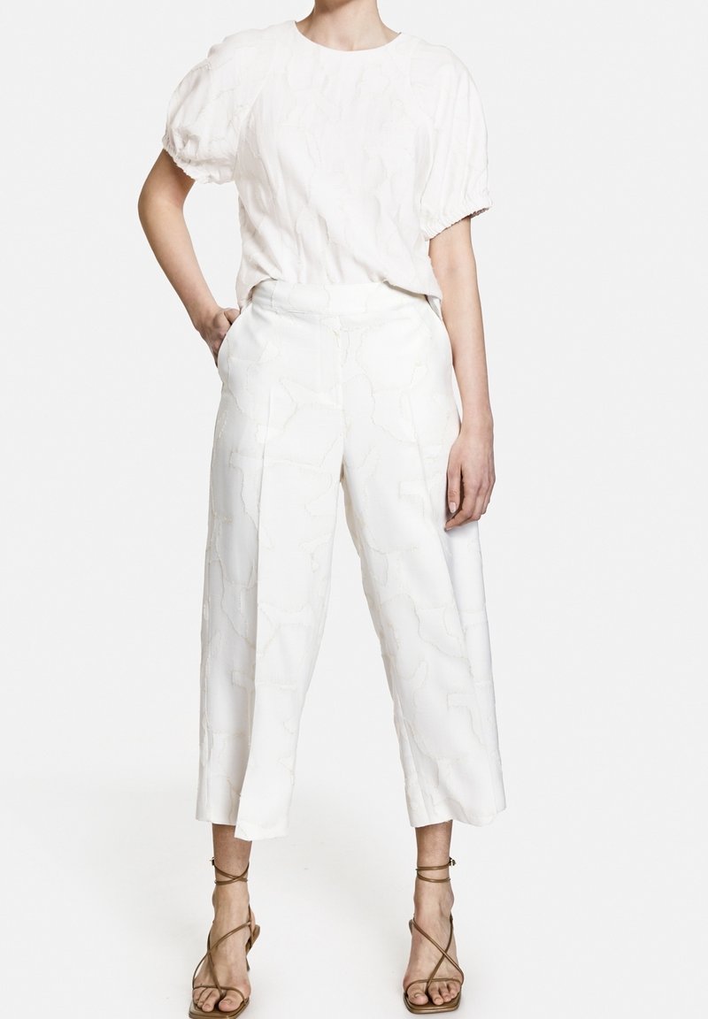 Biała teksturowana bluzka z krótkimi bufkami zestawiona z białymi, szerokimi spodniami o subtelnym wzorze. Sandały na cienkich paskach w kolorze brązowym.