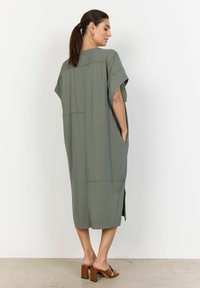 Luźna sukienka kaftan w jasnym oliwkowym zielonym kolorze, z krótkimi rękawami, bocznymi kieszeniami i długością poniżej kolan z bocznymi rozcięciami.
