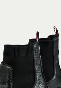 Schwarze Knöchelbooties aus strukturiertem Leder mit dehnbarem Rippstoff. Mit farbigen Zuglaschen und einem eleganten Design.