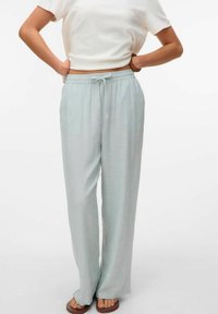 Lichtgroene, comfortabele broek van zachte stof met een verstelbare taille en wijde pijpen, gecombineerd met een eenvoudig wit shirt met korte mouwen.