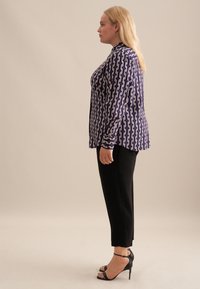 Blusa a fantasia viola e bianca con design a bottoni, abbinata a pantaloni neri a sigaretta e sandali con tacco alto. Tessuto dal tocco morbido.