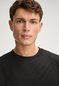 Felpa nera con un motivo testurizzato, colletto rotondo e polsini a costine. Finitura in tessuto liscia con dettagli sottili.