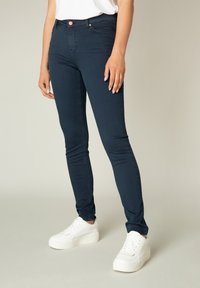 Donkerblauwe skinny jeans met een gladde textuur, voorzien van een knoopsluiting en een vijf-pocket ontwerp, gecombineerd met witte platform sneakers.