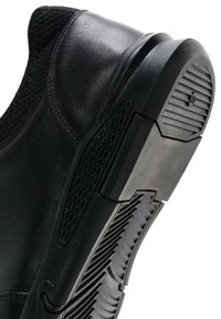 Zapatilla negra con un upper de cuero liso, detalles de malla y una suela de goma texturizada con surcos para tracción y estabilidad.
