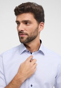 Camicia a fantasia azzurro chiaro con colletto button-down e dettagli blu navy. Presenta un tessuto testurizzato e bottoni blu scuri.