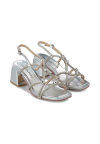 Sandalias de tacón bloque plateadas con correas entrecruzadas. Parte superior metálica suave con adornos de cuentas y diseño de punta cuadrada.