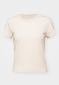 Kortärmad beige t-shirt i bomull med rund halsringning och Nike-logotyp i ljusgrått ovanför bröstet. Slät textur.
