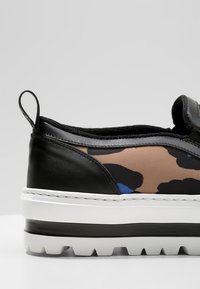 Czarne wsuwane sneakersy z wzorem w kamuflaż w odcieniach brązu, beżu i niebieskiego. Gruba biała podeszwa z teksturowanym gripem oraz pętelka z tyłu.