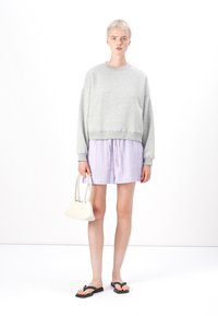 Sweatshirt en coton gris, shorts à rayures légères, tongs noires et un petit sac à main blanc. Le modèle se tient contre un fond blanc.