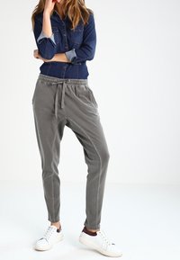 Graue Jogginghosen mit elastischem Bund und Kordelzug, kombiniert mit einem dunkelblauen Jeanshemd und weißen Sneakers. Glatte Stoffstruktur.