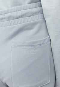 Svetle modré tepláky s přišitou zadní kapsou s jemným logem a hladkou, měkkou texturou látky.