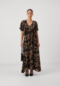 Maxikjole med V-hals, flagrende ærmer og elastisk liv. Mønstret i sorte og brune bølger, parret med en sort taske og sko.