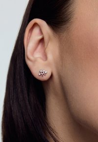 Srebrne kolczyki w kształcie drzewka z akcentami kamieni szlachetnych, zaprezentowane na zbliżeniu ucha i gładkiej strukturze skóry.