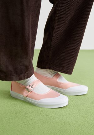 Roze canvas schoenen met een ronde neus, voorzien van een zilveren gesp sluiting en witte rubberen zolen, gedragen met witte sokken en bruine corduroy broek.