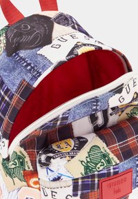 Batoh s designem patchwork, který kombinuje denim a kárované vzory. Červený vnitřek, zapínání na zip a značková etiketa. Červené popruhy.