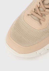 Μπεζ υφασμάτινο μπροστινό μέρος αθλητικού παπουτσιού με κορδόνια στο ίδιο χρώμα και ανοιχτόχρωμη λαστιχένια σόλα, που εμφανίζει υφή πλέξης και συνθετικές επι καλύψεις.