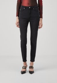 Svarte denimjeans med slim fit, fem lommer og subtile sømdetaljer, kombinert med spisse svarte hæler med gullfinesser.