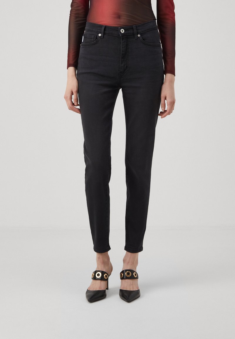 Svarte denimjeans med slim fit, fem lommer og subtile sømdetaljer, kombinert med spisse svarte hæler med gullfinesser.