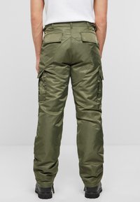 Pantalons cargo en vert olive, fabriqués dans un tissu lisse et brillant. Le design comprend de grandes poches latérales et une forme de jambe fuselée.
