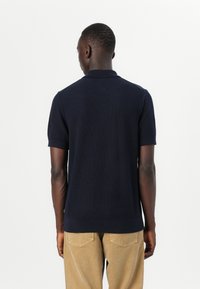 Cămașă polo navy cu mânecă scurtă, dintr-un material texturat și cu un guler clasic, asortată cu pantaloni bej; design simplu cu croială dreaptă.