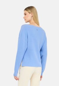 Maglione azzurro chiaro lavorato a maglia con scollo ampio e spacchi laterali. Presenta un piccolo dettaglio con bottoni sul retro e una vestibilità comoda.