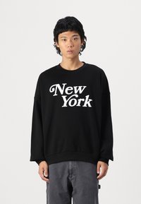 Čierna mikina s nápisom "New York" potlačeným bielou farbou, spájajúca okrúhly výstrih a dlhé rukávy. Hladká textura, uvoľnený strih.