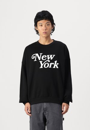 Černá mikina se středním výstřihem a dlouhými rukávy, na které je vytištěno "New York" bílými písmeny. Hladká textura, volný střih.
