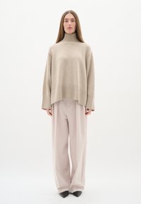 Beige pletený rolák se žebrovým lemem, zkombinovaný s světle růžovými kalhotami s širokými nohavicemi a černými špičatými botami na neutrálním pozadí.