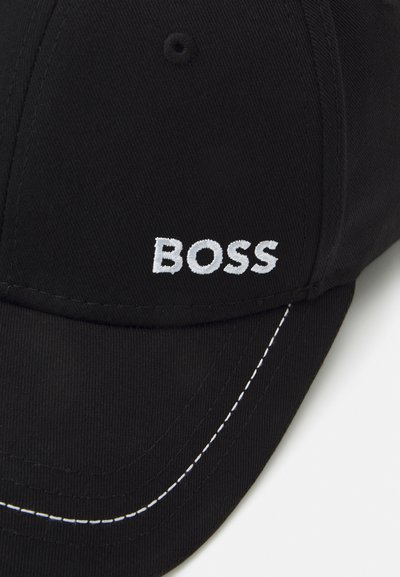 Casquette noire en tissu texturé avec une visière courbée, des coutures décoratives et un logo "BOSS" brodé en blanc.