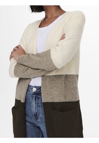 Polven mittainen neuletakki kermansävyssä, taupessa ja tummanruskeana, rento istuvuus, avoin etuosa ja kaksi etutaskua. Pehmeä pinta.