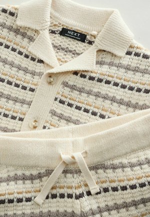 Neulottu oloasu sarja kermaan sävyssä, jossa on beigejä, ruskeita ja harmaita raitoja. Sisältää kauluksellisen yläosan, jossa on napillinen suljenta ja kiristysnyörillä varustettu vyötärö.