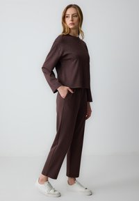 Bruine lange mouwen top met studs gecombineerd met bijpassende broek, met een relaxte pasvorm en zakken, aangevuld met witte sneakers.