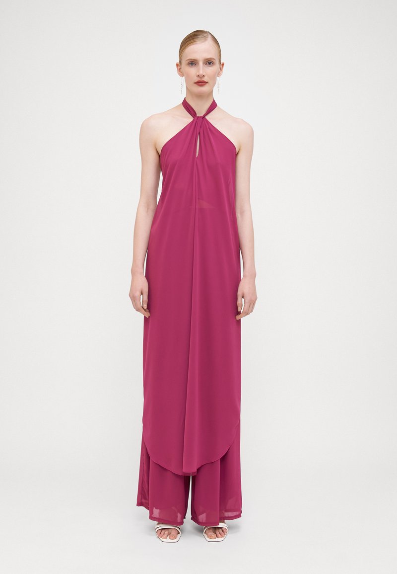 Robe longue à dos nu en chiffon rose vif. Présente un détail en forme de clé et un design superposé. Tissu fluide créant de douces drapés.