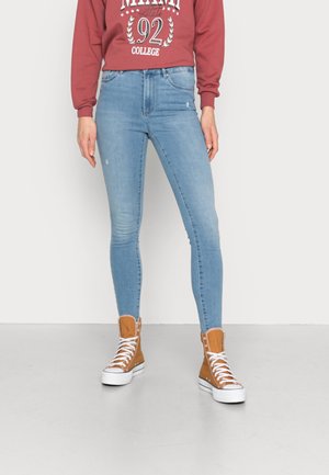 Vaqueros ajustados de color azul claro con un ligero desvanecimiento y detalles desgastados, combinados con zapatillas altas color tostado que tienen suelas y cordones blancos.