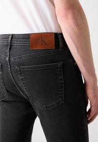 Jeans ajustados negros hechos de denim, con una etiqueta de cuero de Calvin Klein en la parte posterior y detalles de costura sutiles en los bolsillos.