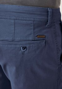 Navy blue trousers with a textured fabric, featuring a back pocket with a button closure and a small branded metal accent.