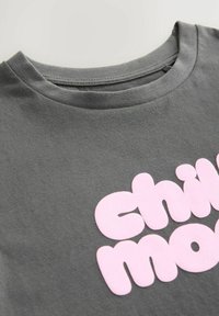 Szürke pamut póló, kerek nyakkivágással és egy nagy, stilizált rózsaszín nyomtatott szöveggel, amely így olvasható: "chill mode."