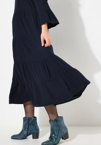 Marineblauwe tiered jurk met uitlopende mouwen en zwarte panty's; draagt blauwe slangenhuid enkellaarsjes met een chunky hak en gestructureerd patroon.