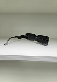 Lunettes de soleil rectangulaires noires avec des verres foncés, une finition brillante et une monture large et robuste. Présente un logo sur la branche latérale.