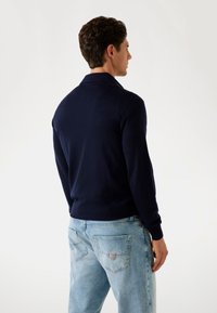 Navyblauer gestrickter Pullover mit Kragen, langen Ärmeln und schmalem Saum. Trägt man über hellblauen Jeans mit zwei Gesäßtaschen und Logodetail.