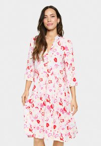 Robe florale avec un fond rose et crème clair, mettant en avant des fleurs rouges et roses, un décolleté en V, des manches trois-quarts et un ourlet évasé.
