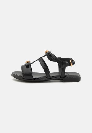 Black flat sandals with multiple straps, made of smooth synthetic material, featuring gold-tone accents and a minimalistic design.