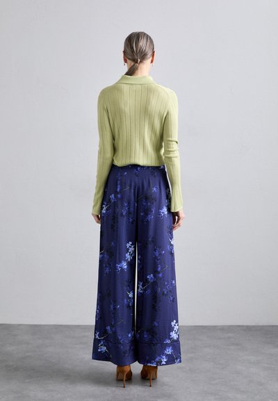 Light green ribbed sweater paired with navy floral wide-leg pants featuring blue and white flower patterns and brown high-heeled shoes.