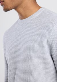 Light grey sweater with a textured, waffle-knit pattern. Features a round neckline and ribbed cuffs for a snug fit.